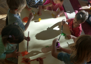 Dzieci siedzące przy stole malują folię bąbelkową farbą